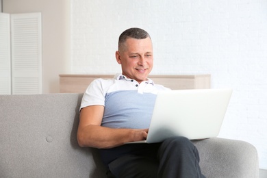 Mature man with laptop sitting on sofa at home