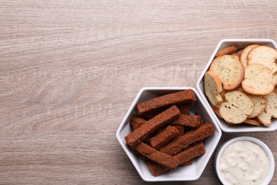 Photo of Different crispy rusks and dip sauce on wooden table, flat lay. Space for text