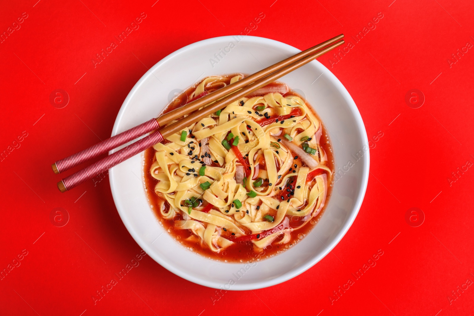 Photo of Plate of asian noodles with broth, vegetables and chopsticks on color background, top view