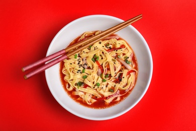 Plate of asian noodles with broth, vegetables and chopsticks on color background, top view