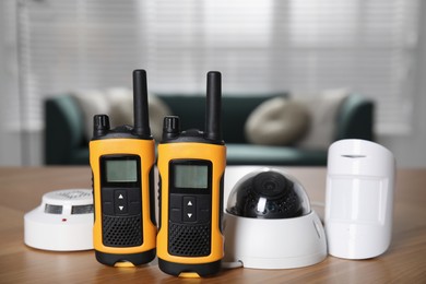 Photo of CCTV camera, walkie talkies, smoke and movement detectors on wooden table indoors. Home security system