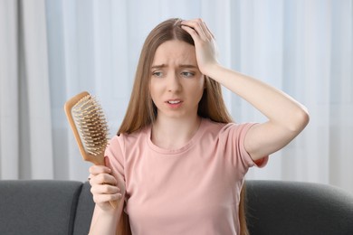 Emotional woman holding brush with lost hair at home. Alopecia problem