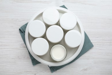 Modern yogurt maker with full jars on white wooden table, top view