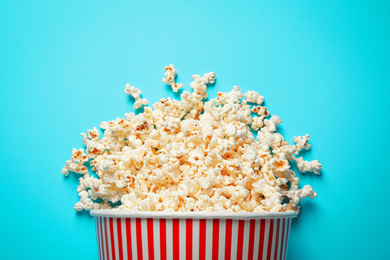 Photo of Overturned paper bucket with delicious popcorn on light blue background, top view