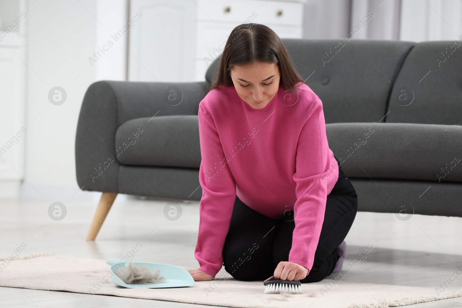 Photo of Woman with brush removing pet hair from carpet at home