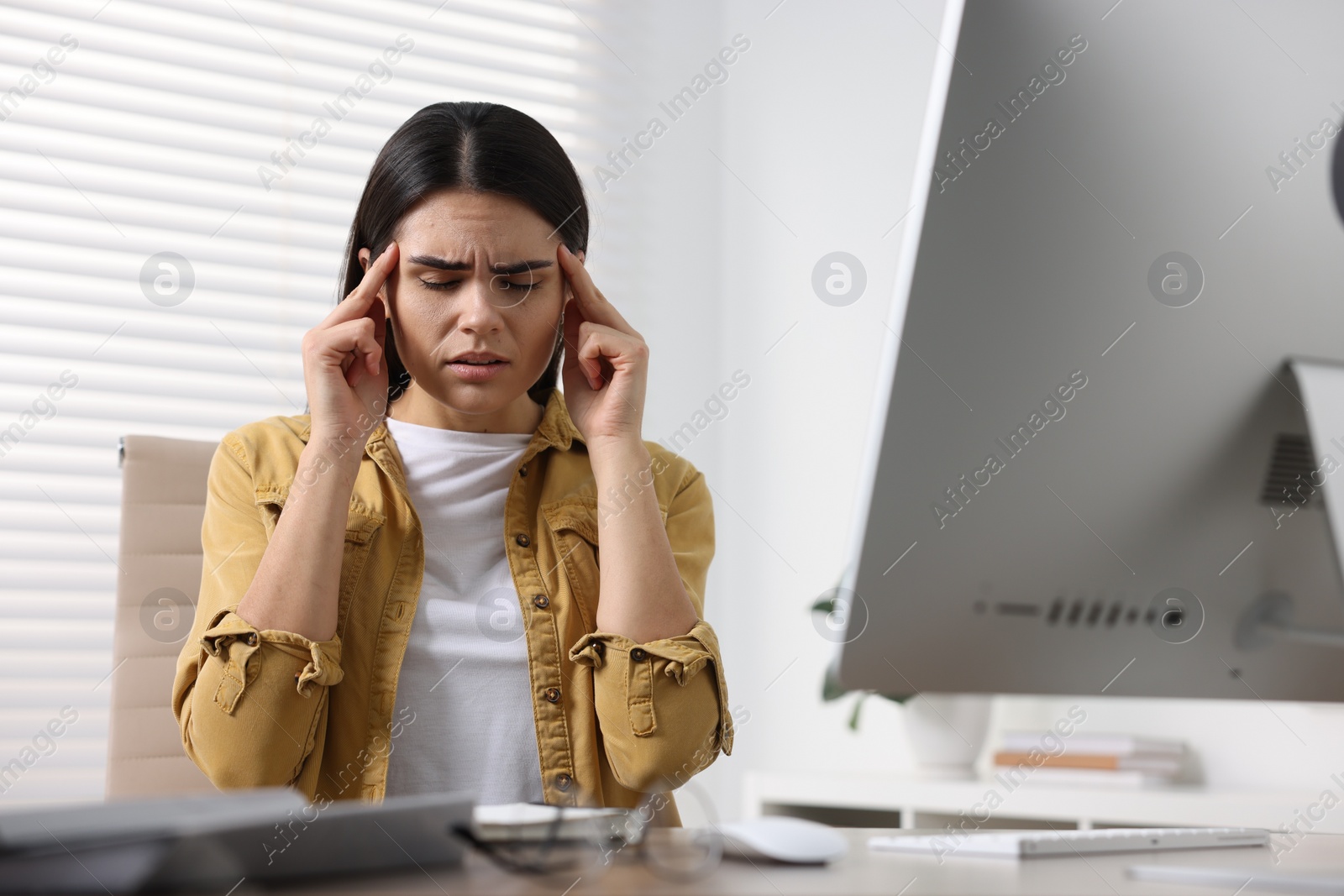 Photo of Young woman suffering from headache at wooden table in office