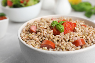 Tasty buckwheat porridge with sausages on table, closeup