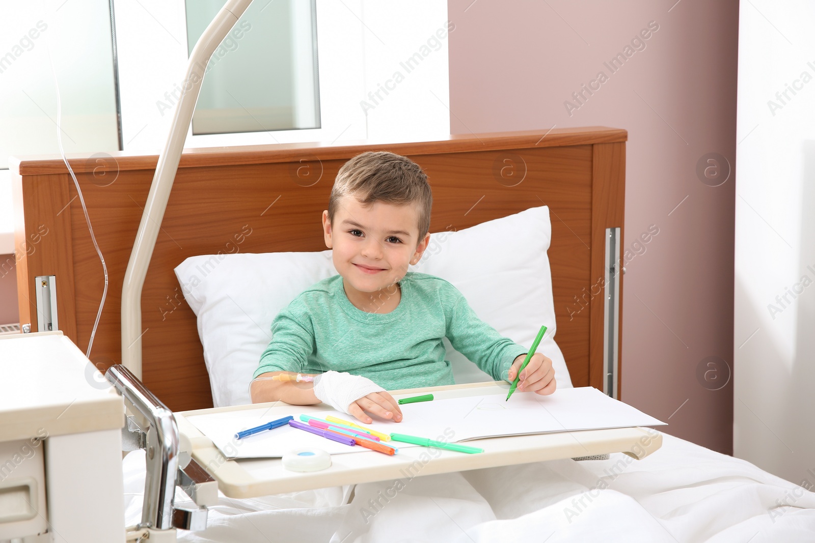 Photo of Little child with intravenous drip drawing in hospital bed