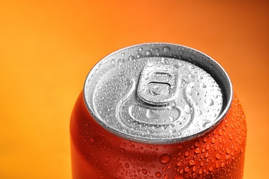 Photo of Aluminum can of beverage covered with water drops on orange background, closeup. Space for text