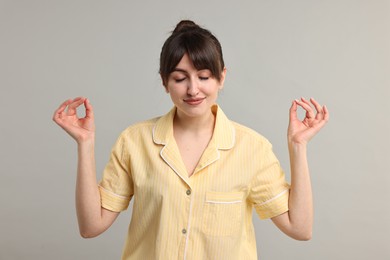 Woman in pyjama meditating on grey background