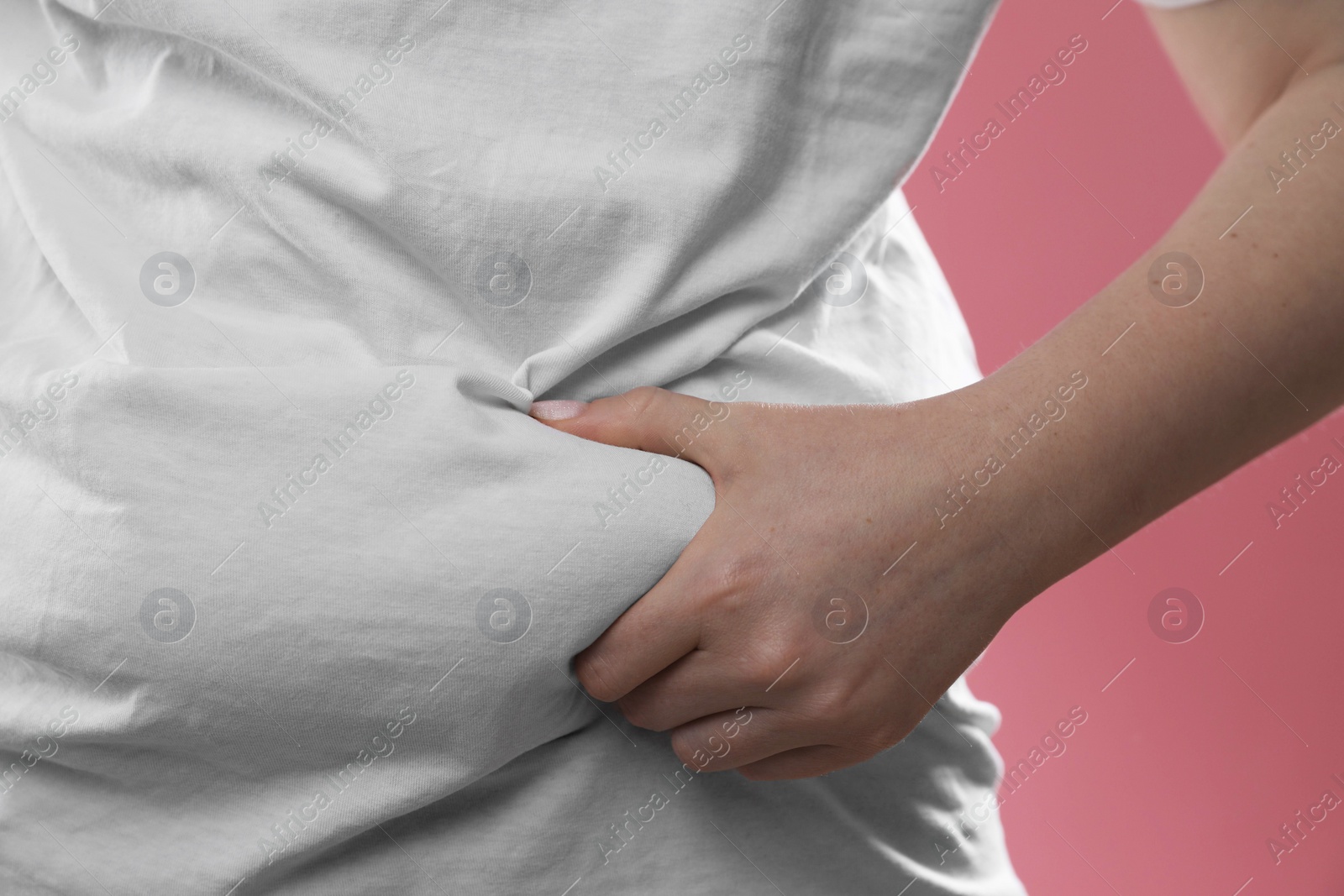 Photo of Woman touching belly fat on pink background, closeup. Overweight problem