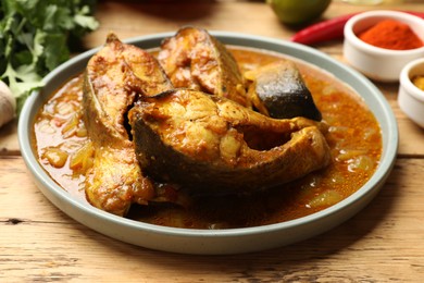 Photo of Tasty fish curry on wooden table, closeup. Indian cuisine
