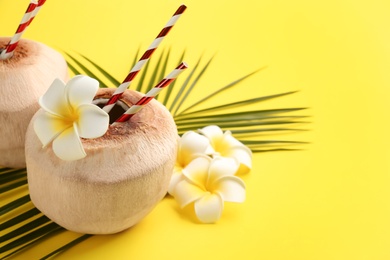 Photo of Fresh coconuts with drinking straws and flowers on yellow background. Space for text