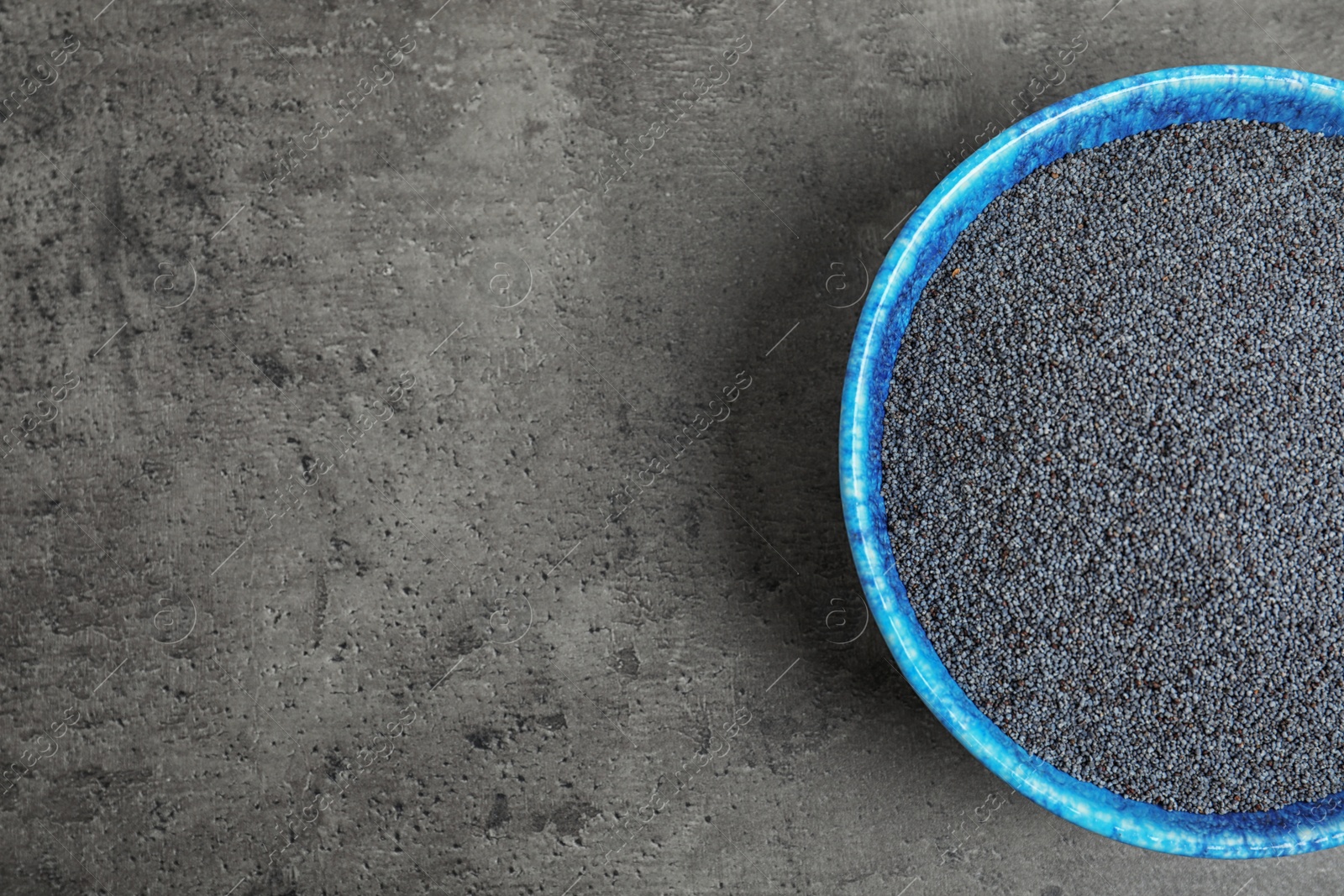 Photo of Poppy seeds in bowl and space for text on grey background, top view