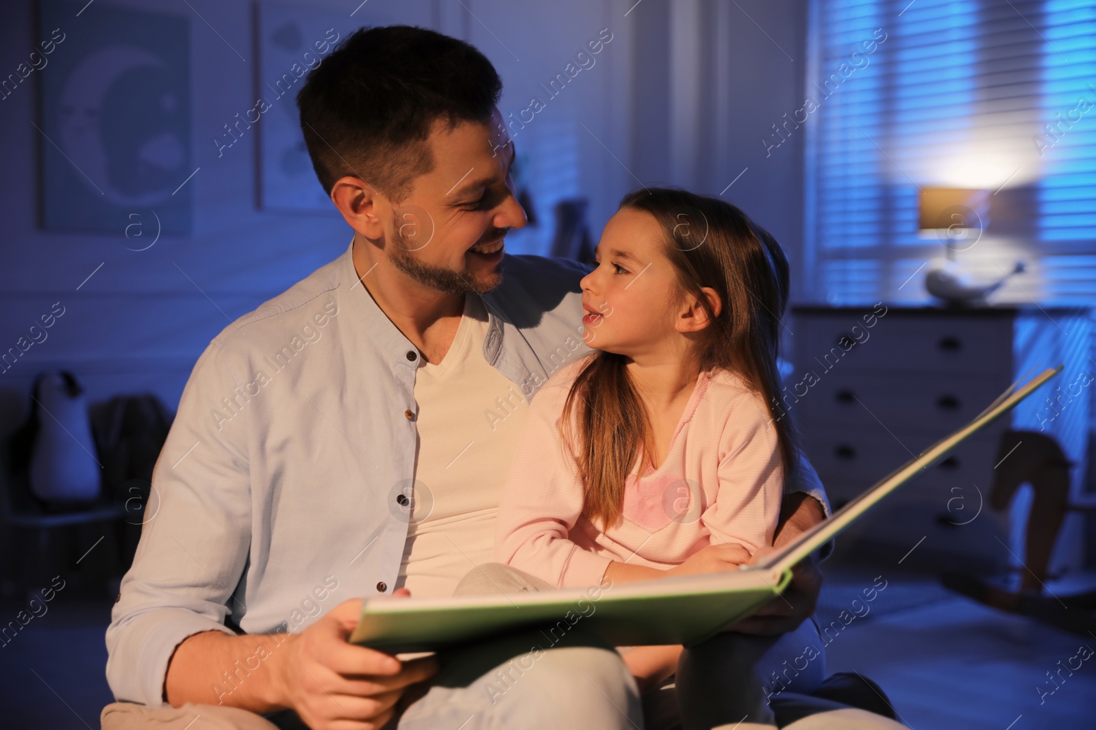 Photo of Father reading bedtime story to his daughter at home