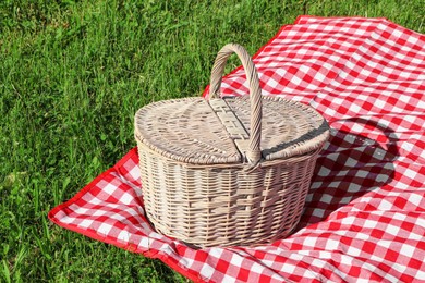 Picnic basket with checkered tablecloth on green grass outdoors