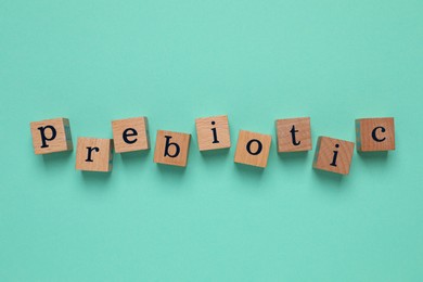 Photo of Wooden cubes with word Prebiotic on turquoise background, flat lay