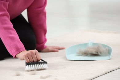 Photo of Woman with brush removing pet hair from carpet at home, closeup