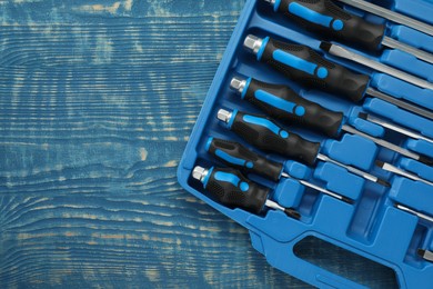 Photo of Set of screwdrivers in open toolbox on blue wooden table, top view. Space for text