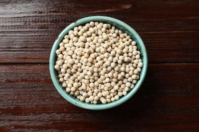 Aromatic spice. White pepper in bowl on wooden table, top view