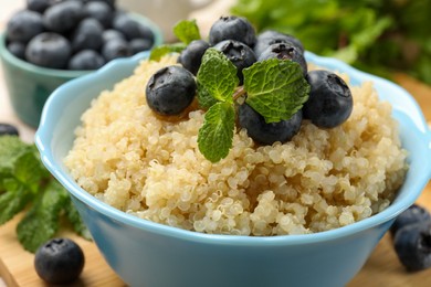 Photo of Tasty quinoa porridge with blueberries and mint in bowl on table, closeup