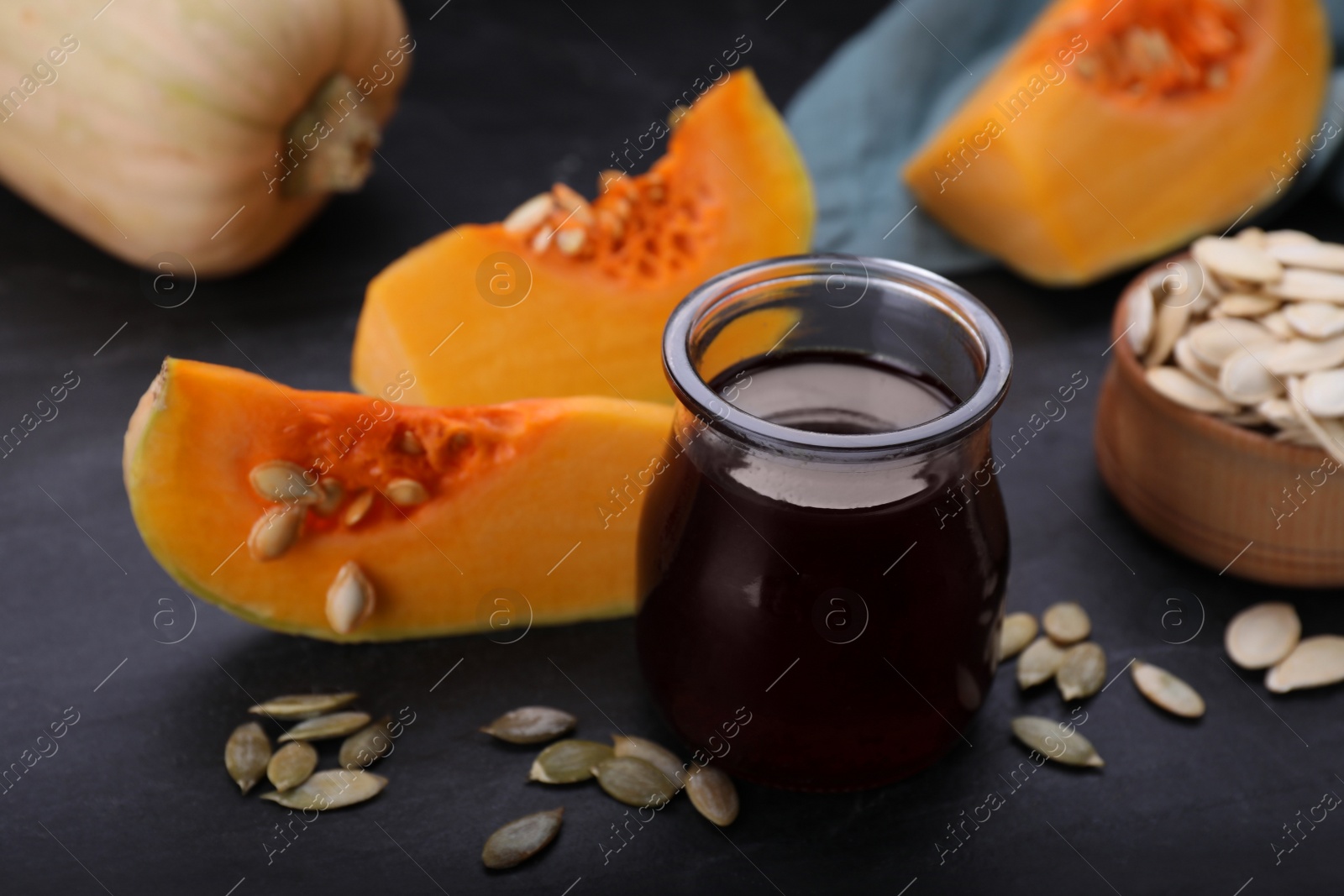 Photo of Fresh pumpkin seed oil in glass jar on dark grey table