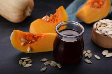 Photo of Fresh pumpkin seed oil in glass jar on dark grey table