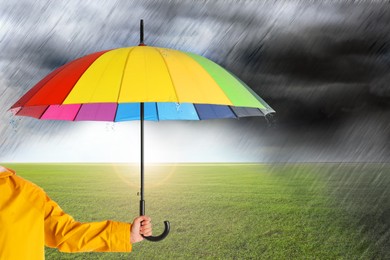 Image of Woman with open bright umbrella under heavy rain in green field, closeup