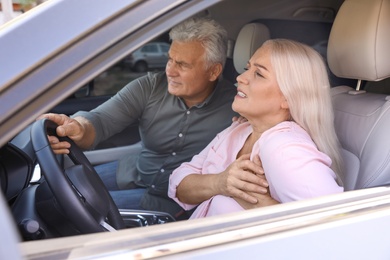 Photo of Senior man holding steering wheel while his wife having heart attack in car