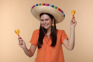 Photo of Young woman in Mexican sombrero hat with maracas on beige background