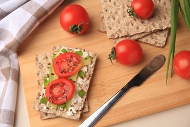 Photo of Fresh crunchy crispbreads with cream cheese, tomatoes and avocado on beige table, above view