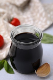 Glass jar with balsamic vinegar, basil, tomatoes and garlic on white table, closeup