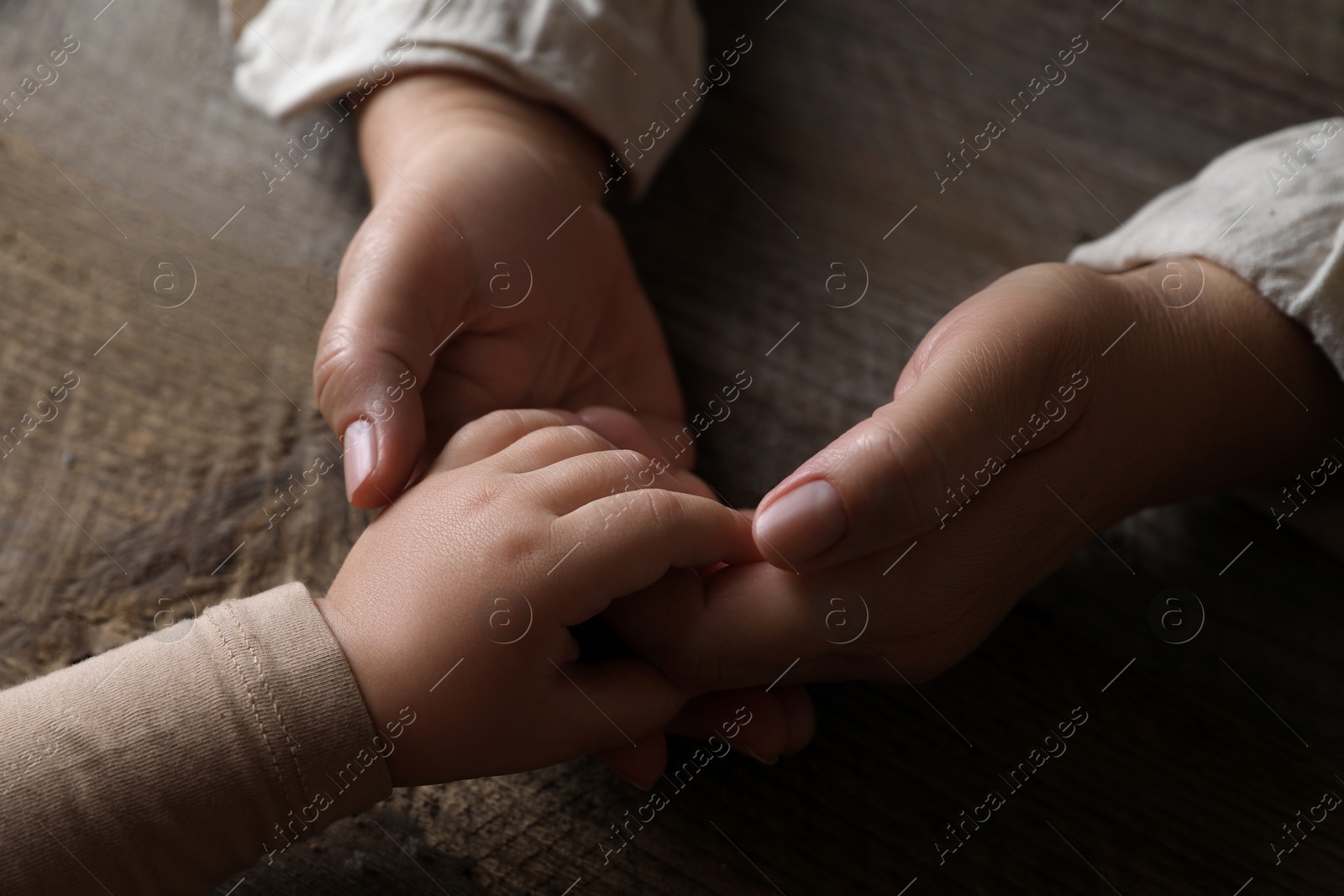 Photo of Woman holding hands with her granddaughter at wooden table, closeup