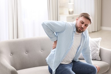 Photo of Man suffering from back pain at home. Bad posture problem