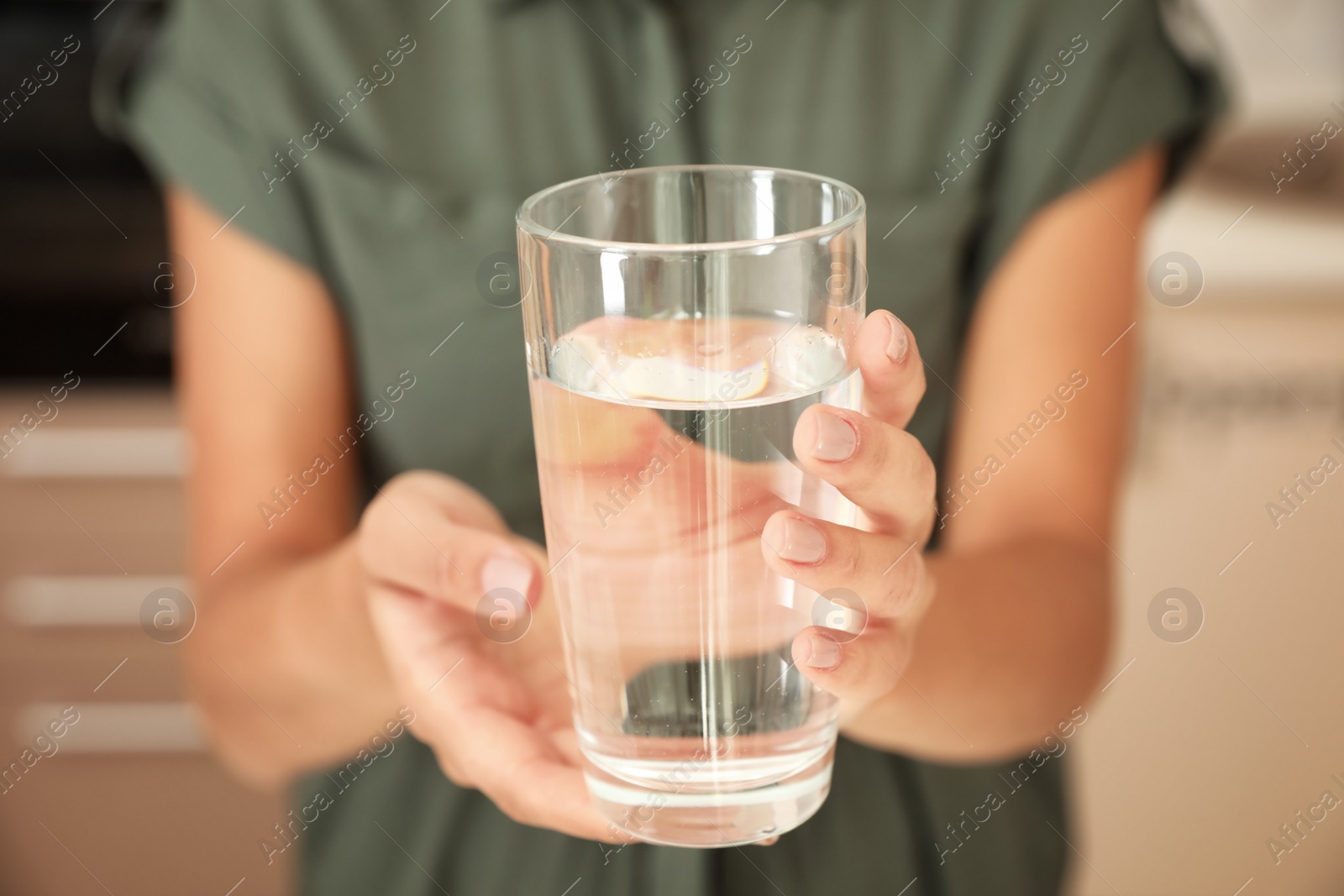 Photo of Woman holding glass with pure water in kitchen, closeup