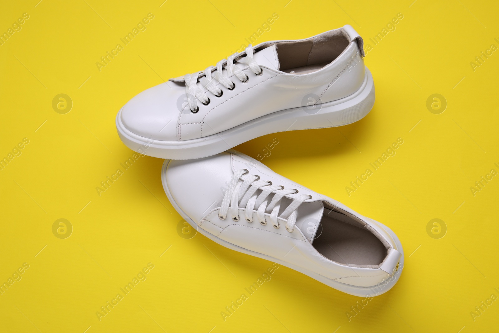 Photo of Pair of stylish white sneakers on yellow background, top view