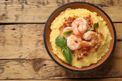 Photo of Fresh tasty shrimps, bacon, grits and basil in bowl on wooden table, top view. Space for text