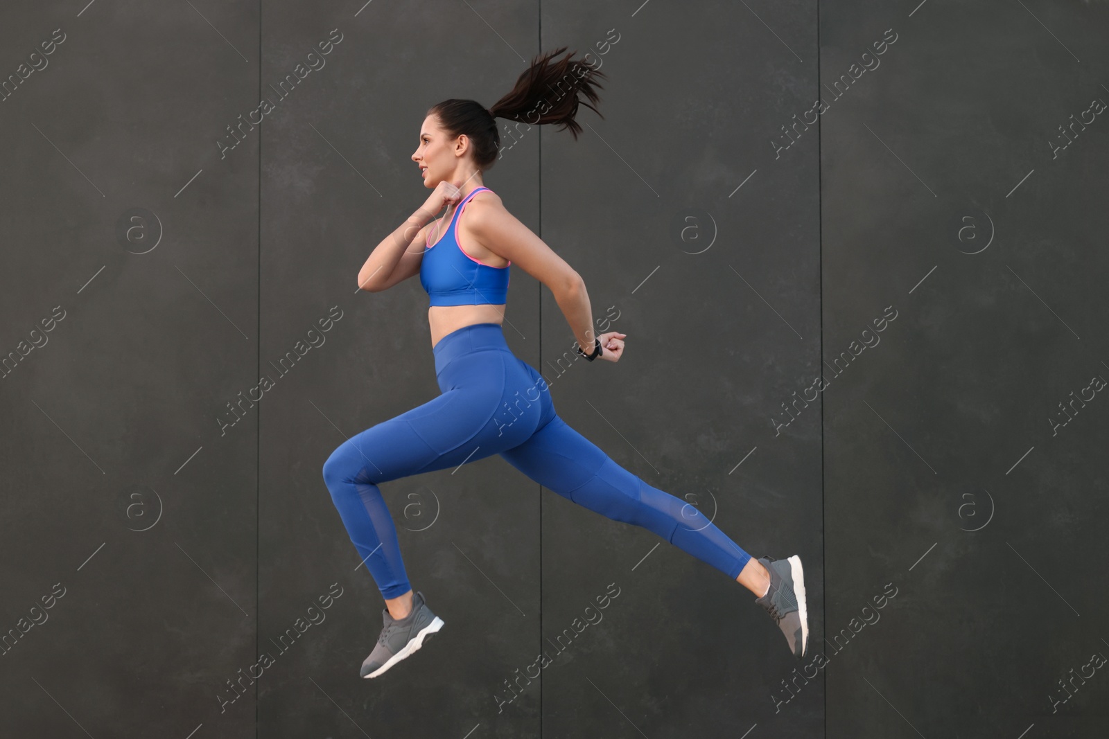 Photo of Beautiful woman in stylish sportswear jumping near black wall, space for text