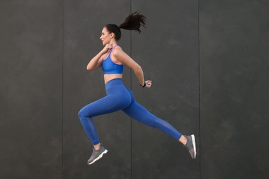 Beautiful woman in stylish sportswear jumping near black wall, space for text