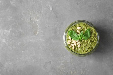 Jar with delicious pesto sauce, pine nuts and basil leaves on grey table, top view. Space for text