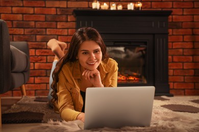 Photo of Young woman with laptop on floor near fireplace at home