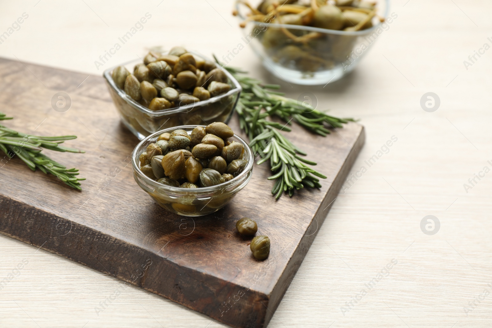 Photo of Delicious pickled capers and rosemary twigs on white wooden table, space for text