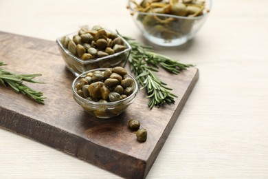 Photo of Delicious pickled capers and rosemary twigs on white wooden table, space for text