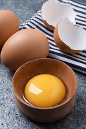 Photo of Raw chicken eggs and bowl with yolk on grey table, closeup
