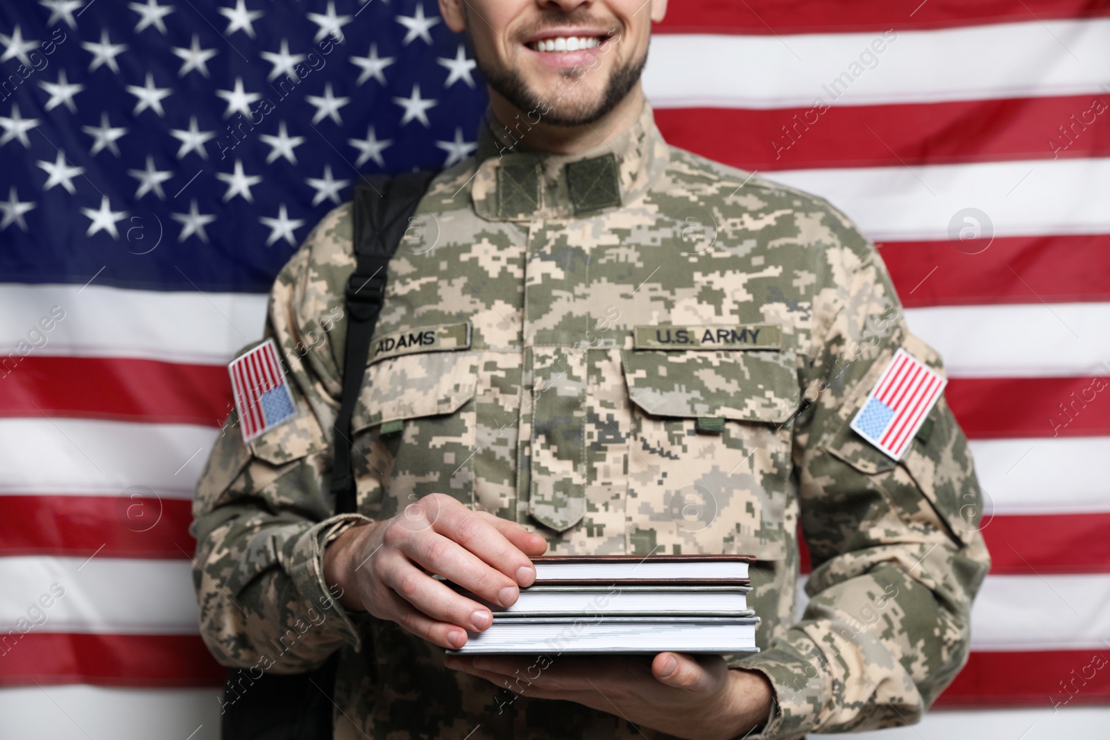 Photo of Cadet with backpack and books against American flag, closeup. Military education