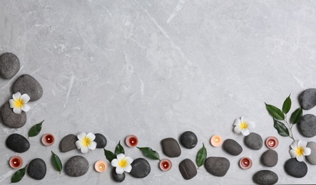 Flat lay composition with spa stones and lit candles on grey marble background, space for text