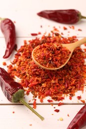 Photo of Chili pepper flakes and pods on white wooden table, closeup