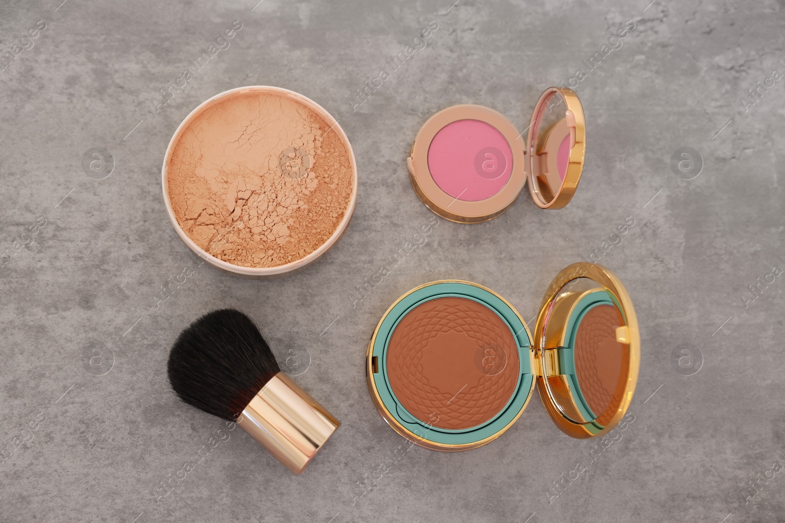 Photo of Bronzer, powder, blusher and brush on grey textured table, flat lay