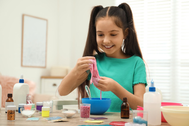 Cute little girl making DIY slime toy at table indoors