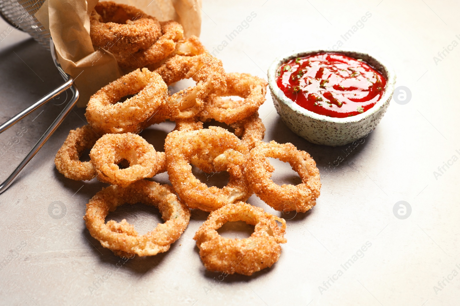 Photo of Homemade crunchy fried onion rings and tomato sauce on light background